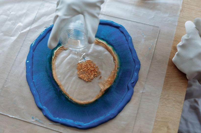 Gloved hands pouring blue resin with a gold centre